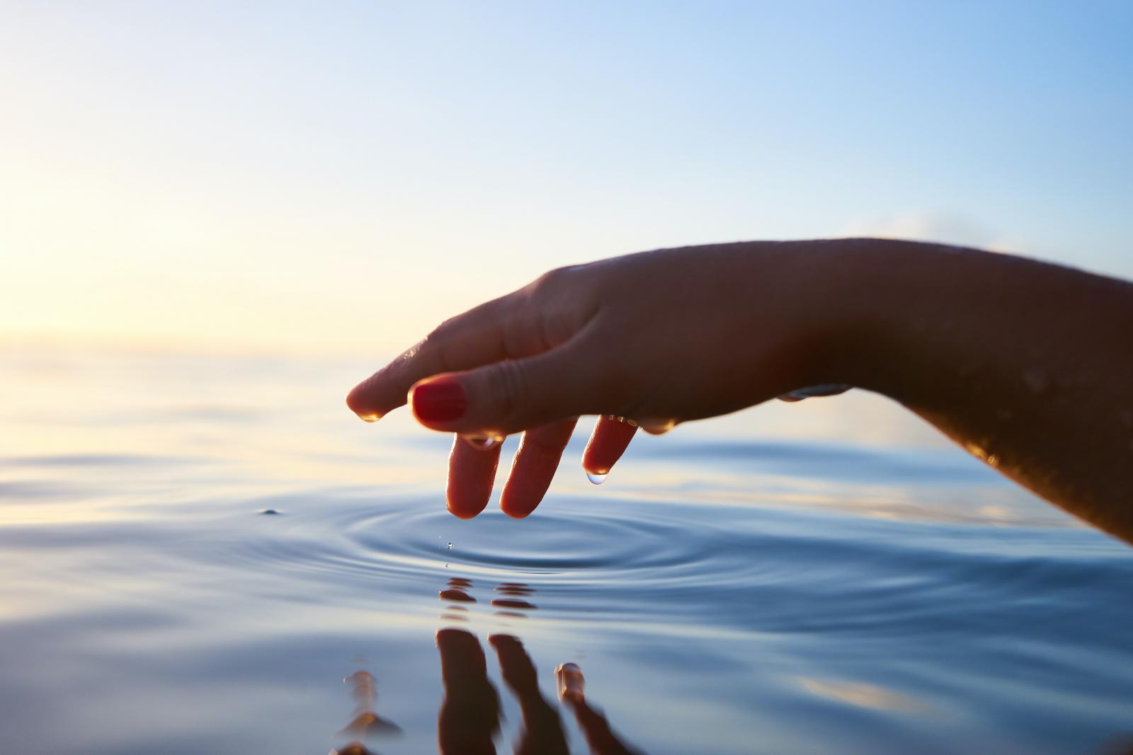 Mano di donna che sfiora superficie di acqua  