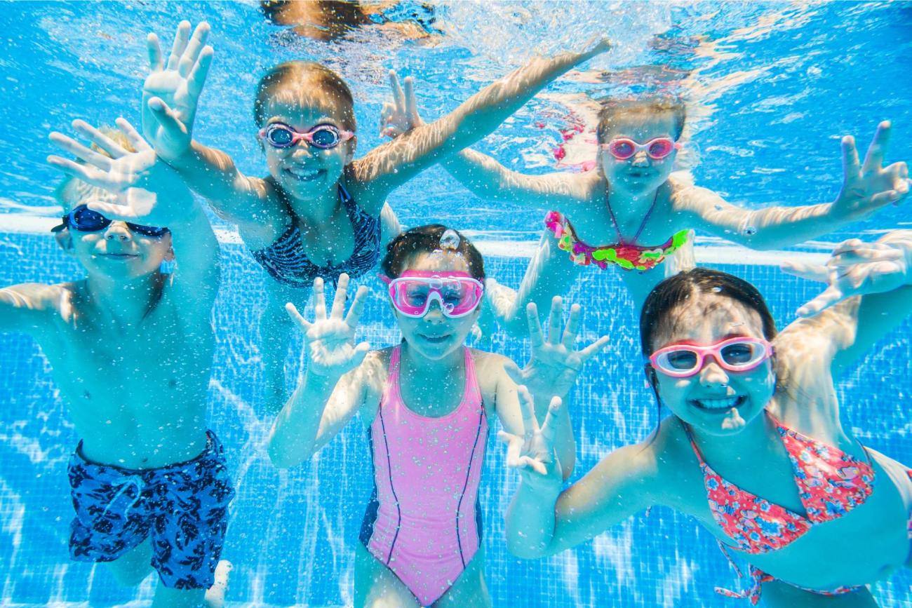 Gruppo di bambini sorridenti sott’acqua in piscina