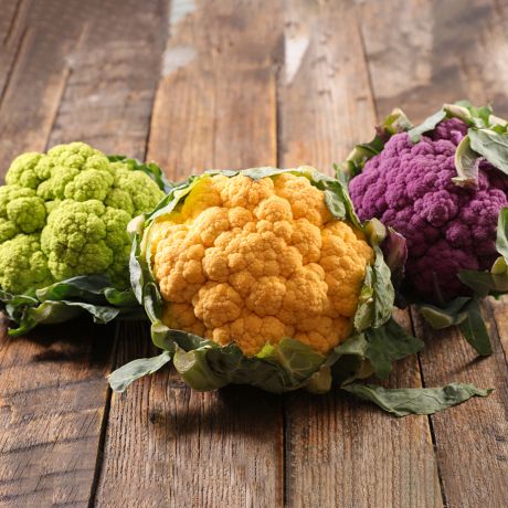 Cime di cavolfiore giallo, verde e viola su tavola di legno