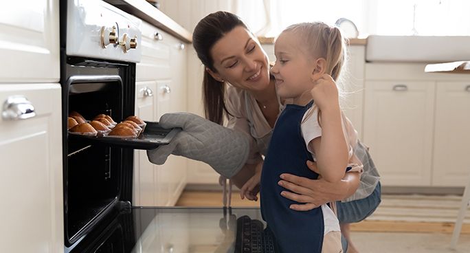 la bambina con le trecce indossa il grembiule, impara a cucinare, posa  vicino ai fornelli, prepara le uova fritte per la colazione, aiuta i  genitori a cucinare, è impegnata nella cucina moderna.