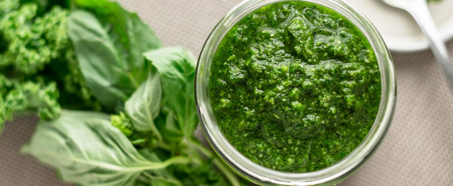 Pesto in barattolo di vetro con accanto un ramo di basilico fresco